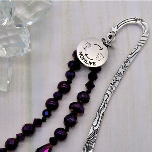 May include: Silver bookmark with a purple beaded tassel and a round charm that says "Momlife" with a wine glass and coffee cup graphic.