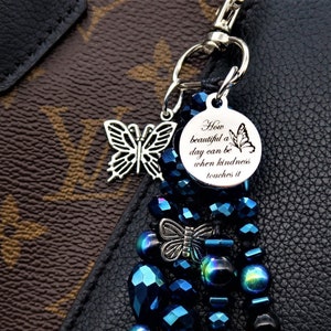 May include: A blue and black beaded keychain with a silver charm that says "How beautiful a day can be when kindness touches it".
