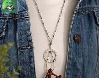 May include: A silver-toned metal necklace featuring a textured circular pendant with a smooth teardrop-shaped loop attached at the bottom. The necklace is worn over a white shirt and a blue denim jacket. The text Crafted by Kristal is visible.