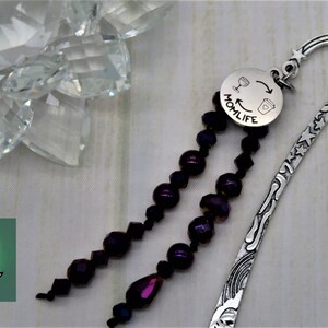 May include: Silver bookmark with a purple beaded tassel and a round charm that says "Momlife" with a wine glass and coffee cup graphic.