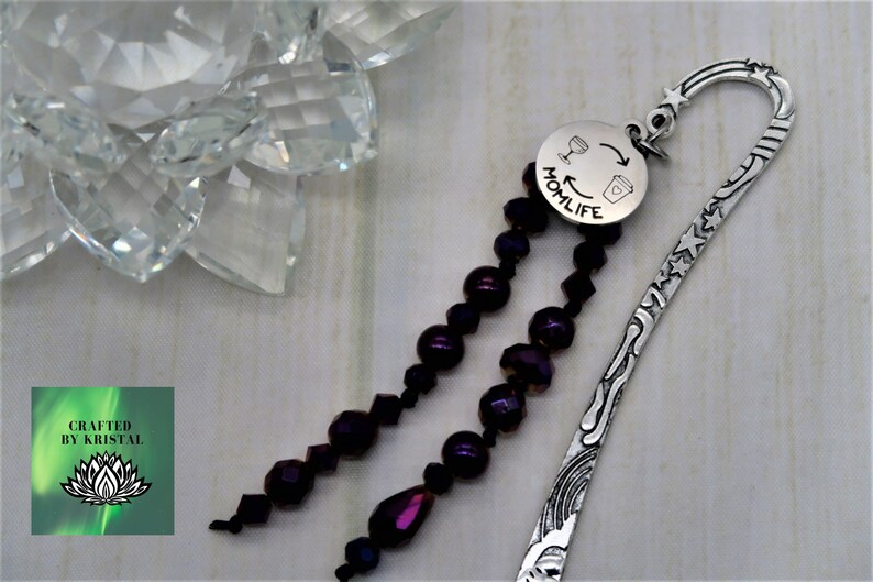 May include: Silver bookmark with a purple beaded tassel and a round charm that says "Momlife" with a wine glass and coffee cup graphic.