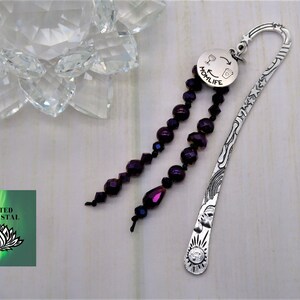 May include: Silver bookmark with a purple beaded tassel. The bookmark is engraved with a sun, stars, and a rainbow. The tassel is attached to a round charm that says "Momlife" with a wine glass and coffee cup graphic.