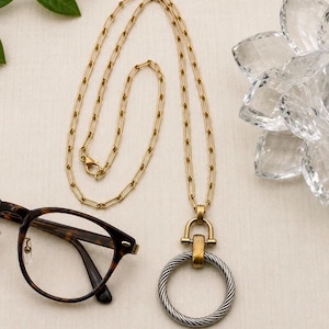 May include: A gold-tone chain necklace with a large silver and gold pendant. The pendant is a twisted silver ring attached to a gold clasp. Tortoiseshell eyeglasses are on the left.