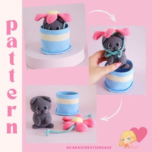 May include: A gray crocheted cat wearing a pink flower pot hat. The cat is sitting in a blue and white striped crocheted pot. The image includes the text "pattern" and "@carascreationsaus".