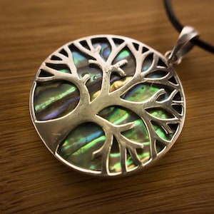 Könnte beinhalten: Ein silberner Lebensbaum-Anhänger mit einer runden Einlage aus Abalone-Muschel. Der Anhänger befindet sich an einer schwarzen Schnur.