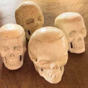 Könnte beinhalten: Vier weiße, geschnitzte Schädelskulpturen, jede mit einem einzigartigen Design und Detail. Die Schädel sind aus einem glatten, elfenbeinartigen Material gefertigt und haben eine leicht gebrochenweiße Farbe.