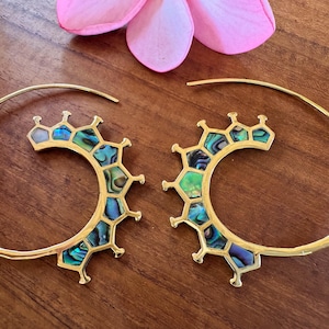 May include: Gold-coloured spiral earrings with a distinctive design. Each earring has a semi-circular shape with a geometric pattern filled with iridescent abalone shell pieces. A pink flower is above.