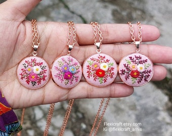May include: Four delicate necklaces with pink embroidered floral pendants on a rose gold chain. Each pendant features a different arrangement of pink, red, white, and blue flowers.