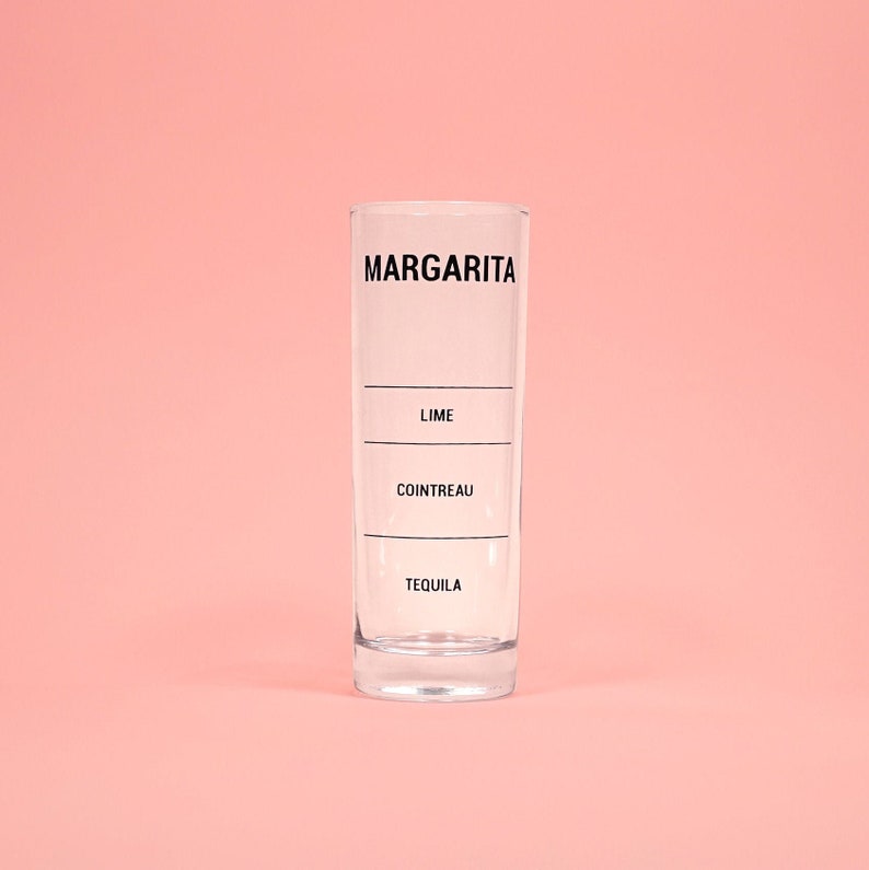 May include: A clear glass margarita measuring cup with black markings for tequila, Cointreau, and lime.