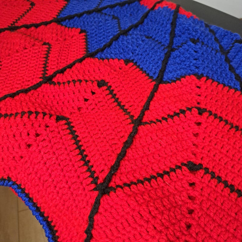 Puede incluir: Una manta de ganchillo hecha a mano con un patr&oacute;n geom&eacute;trico. La manta es principalmente roja con secciones azules y costuras negras que delinean las formas. La textura del hilo es visible, lo que sugiere un art&iacute;culo acogedor y artesanal.