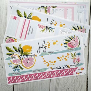 May include: Laurel Denise Large Scout planner sheets with watercolor illustrations of fruit, including lemons and watermelon. The planner sheets have a July theme with dates and notes sections. The text "July" is visible.
