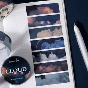 May include: A roll of washi tape with a cloud design. The tape is printed with images of clouds in different shades of blue and pink against a dark blue background. The tape is labeled "CLOUD MASKING TAPE" and "KIMO-CARD".
