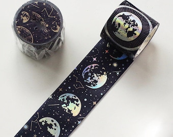 May include: A roll of black washi tape with a holographic moon and star pattern. The tape is unrolled to show the design.