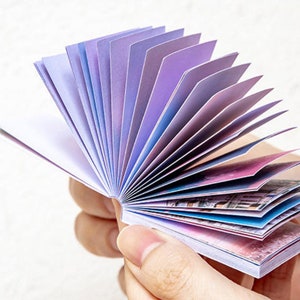 May include: A small, fan-shaped notepad with colorful pages. The pages are decorated with a watercolor-like design of clouds and sky.