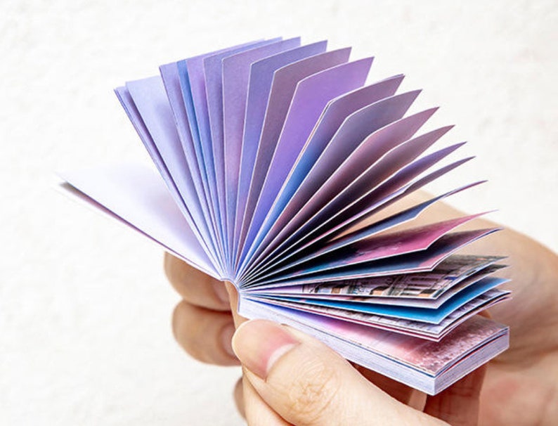 May include: A small, fan-shaped notepad with colorful pages. The pages are decorated with a watercolor-like design of clouds and sky.
