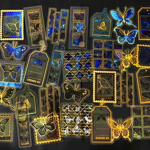 Puede incluir: Un conjunto de 20 pegatinas hologr&aacute;ficas con dise&ntilde;os de mariposas en varios colores, incluidos el azul, el dorado y el negro. Las pegatinas son transparentes y tienen un acabado brillante. Algunas pegatinas tienen texto, incluyendo "Opened By" y "50c".