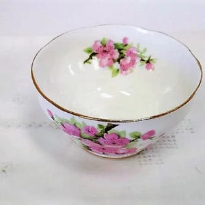 May include: A white porcelain sugar bowl with a gold rim and pink floral design. The bowl has a scalloped edge and is decorated with pink flowers and green leaves.