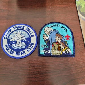 May include: Two embroidered patches. The circular patch is blue and white with a polar bear on an iceberg and the text 'CAMP THREE FALLS POLAR BEAR CLUB'. The arched patch is blue and light blue with a scout illustration, the text 'A SCOUT'S DUTY', '1995', and 'ORANGE COUNTY COUNCIL'.