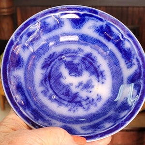 May include: A blue and white porcelain saucer with a decorative floral pattern. The saucer has a scalloped edge and a raised center.