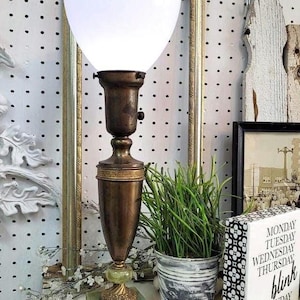 May include: An antique brass table lamp with a white glass shade. The lamp has a decorative base with a green stone accent. A small potted plant and a decorative sign that says "Monday Tuesday Wednesday Thursday blink Monday" are nearby.