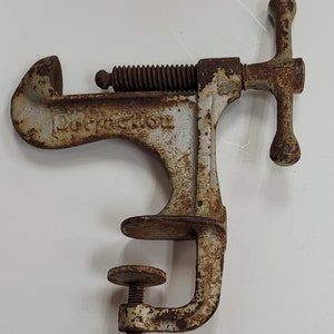 May include: A vintage cast iron Perfection brand nutcracker with a white painted finish and rust patina. The nutcracker has a screw mechanism and a clamp to hold the nut in place.