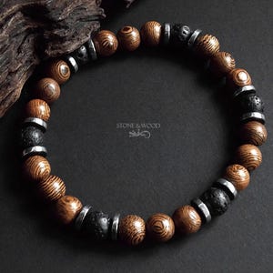 May include: A beaded bracelet featuring alternating round brown wood beads with visible grain, textured black lava stone beads, and smooth metallic silver spacers. The centre of the image displays the text STONE & WOOD with a small lizard icon.