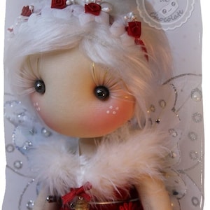 Peut inclure: Une poupée blanche avec des roses rouges dans les cheveux, portant un col en fourrure blanche et une robe rouge avec un charme de bouteille argentée. La poupée a des ailes argentées scintillantes et tient une petite bouteille.