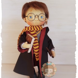 Peut inclure: Une poupée artisanale de Harry Potter, portant une robe noire avec une doublure rouge, une écharpe jaune et marron, et des lunettes rondes. Il tient un livre et une baguette.