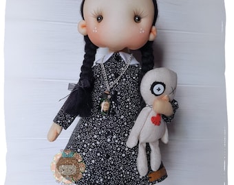 May include: A black and white doll with black hair in pigtails, wearing a black dress with white stars, and holding a white doll with a red heart. The doll is wearing a silver necklace with a charm.