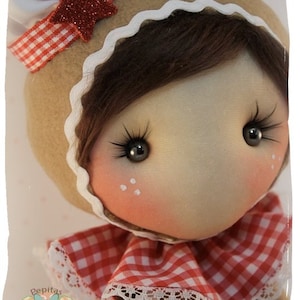 Puede incluir: Una muñeca de jengibre con cabello castaño, vestida con un vestido de cuadros rojos y blancos con ribete de encaje blanco y una diadema roja con forma de estrella. La muñeca tiene una expresión dulce e inocente con ojos marrones y mejillas sonrosadas.