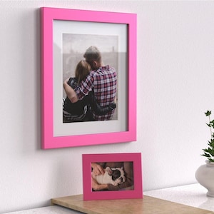 May include: Two pink picture frames, one larger than the other. The larger frame contains a photo of a couple embracing, while the smaller frame contains a photo of a puppy.