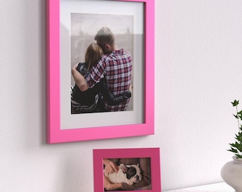 May include: Two pink picture frames, one larger than the other. The larger frame contains a photo of a couple embracing, while the smaller frame contains a photo of a puppy.