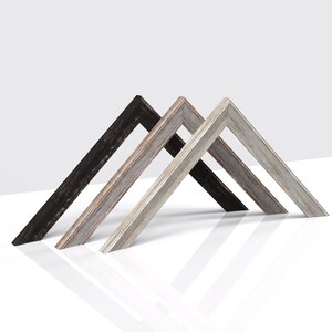 May include: Three picture frames in different wood finishes: black, whitewashed, and grey. The frames are arranged in a triangular shape.