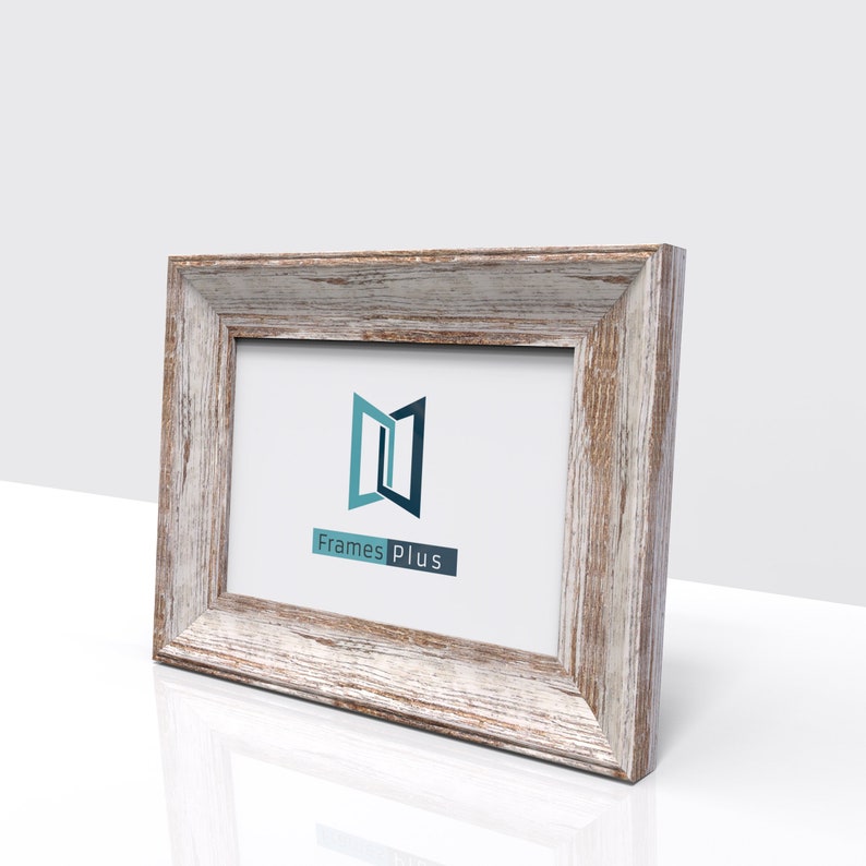 May include: A rustic wood picture frame with a whitewashed finish. The frame has a simple, rectangular design with a slightly raised edge. The frame is empty and ready to display a photo or artwork. The frame is made by Frames Plus.