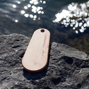 May include: A light brown wooden cutting board with a rounded oval shape and a small hole in the top. The board is sitting on a gray rock.
