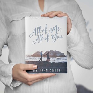 May include: A book cover with the title "All of Me, All of You" by John Smith. The cover features a couple holding hands on a rocky beach.