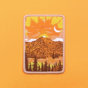 May include: An embroidered patch in a vintage style, depicting a mountain range with a sunset and a crescent moon in the sky. The patch is bordered with a light pink outline.