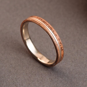 Puede incluir: Primer plano de un anillo con una banda de madera y una fina raya plateada. El anillo está sobre un fondo neutro. El anillo mide aproximadamente 54-3mm.