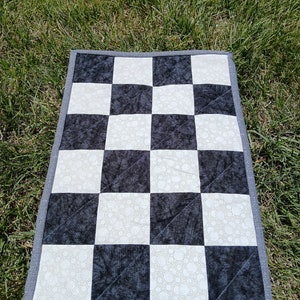 May include: A black and white checkered fabric mat with a gray border. The mat is made of quilted fabric with a white pattern of small circles on the white squares.