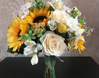 Pode incluir: Um buquê de noiva com girassóis amarelos, rosas brancas e outras flores brancas. O buquê é amarrado com barbante e tem um visual rústico.