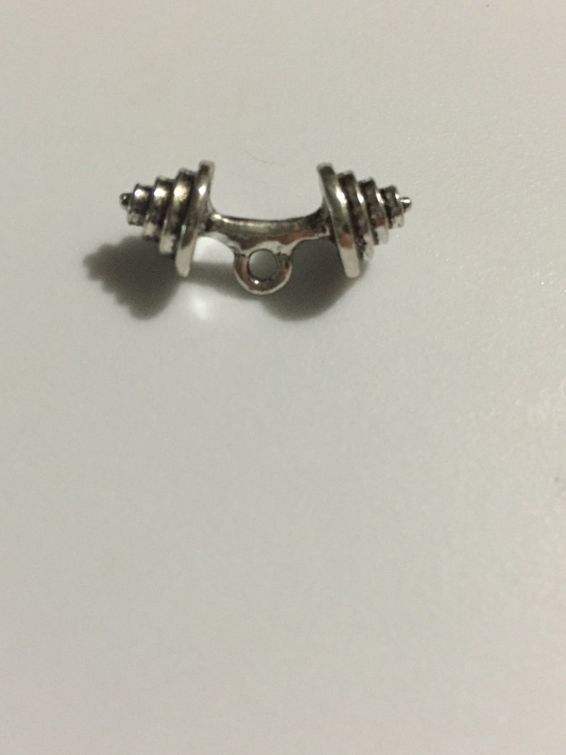 Puede incluir: Encanto de mancuerna de plata con un bucle para sujetarlo a un collar o pulsera.