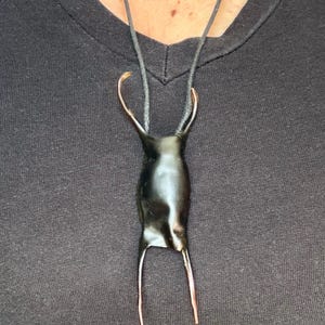 以下が含まれることがあります： 黒いペンダントネックレス。光沢のあるユニークな涙型のチャームと銅色のアクセントが特徴です。チャームは黒いコードから吊り下げられており、暗い背景とのコントラストが際立っています。