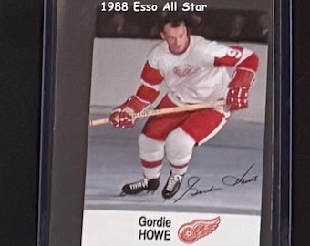 May include: A hockey trading card featuring Gordie Howe, a 1988 Esso All-Star. The card shows Howe in a red and white jersey, holding a hockey stick. The card is in a protective sleeve.