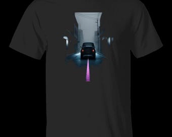 Op de afbeelding: Een zwart t-shirt met korte mouwen en een grafische print van een auto die 's nachts door een donkere, mistige stadsstraat rijdt. De auto staat in het midden met rode achterlichten en een paarse lijn loopt naar de onderkant.