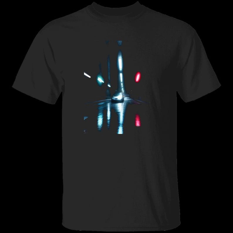 May include: A black short-sleeved t-shirt featuring a central graphic print of a car driving on a wet road at night. The design displays bright white headlights, a glowing teal light on the left, and a vibrant red light on the right side.