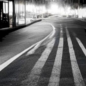 Pode incluir: Uma fotografia a preto e branco de uma estrada de asfalto que se estende na dist&acirc;ncia. A cena apresenta marca&ccedil;&otilde;es de faixa brancas proeminentes que guiam o olhar para uma linha de horizonte brilhante e desfocada.