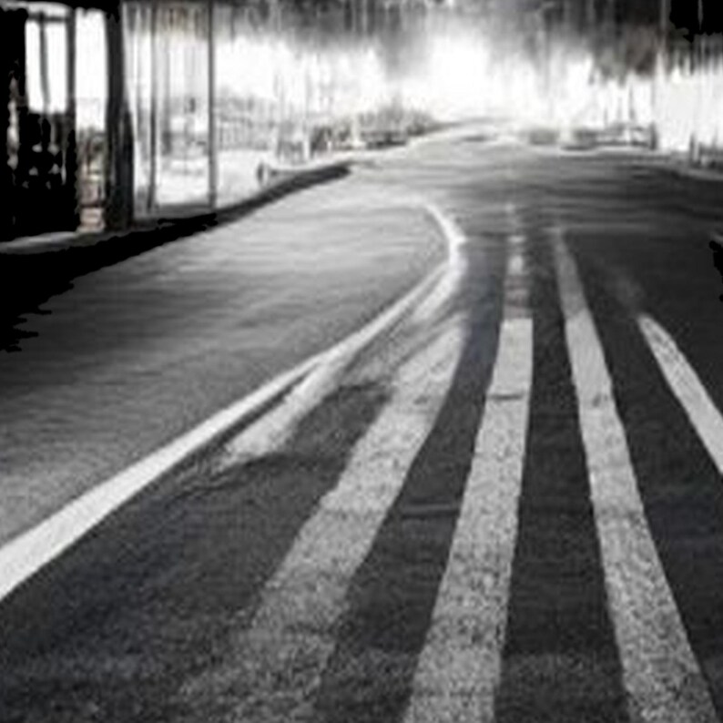 Pode incluir: Uma fotografia a preto e branco de uma estrada de asfalto que se estende na dist&acirc;ncia. A cena apresenta marca&ccedil;&otilde;es de faixa brancas proeminentes que guiam o olhar para uma linha de horizonte brilhante e desfocada.