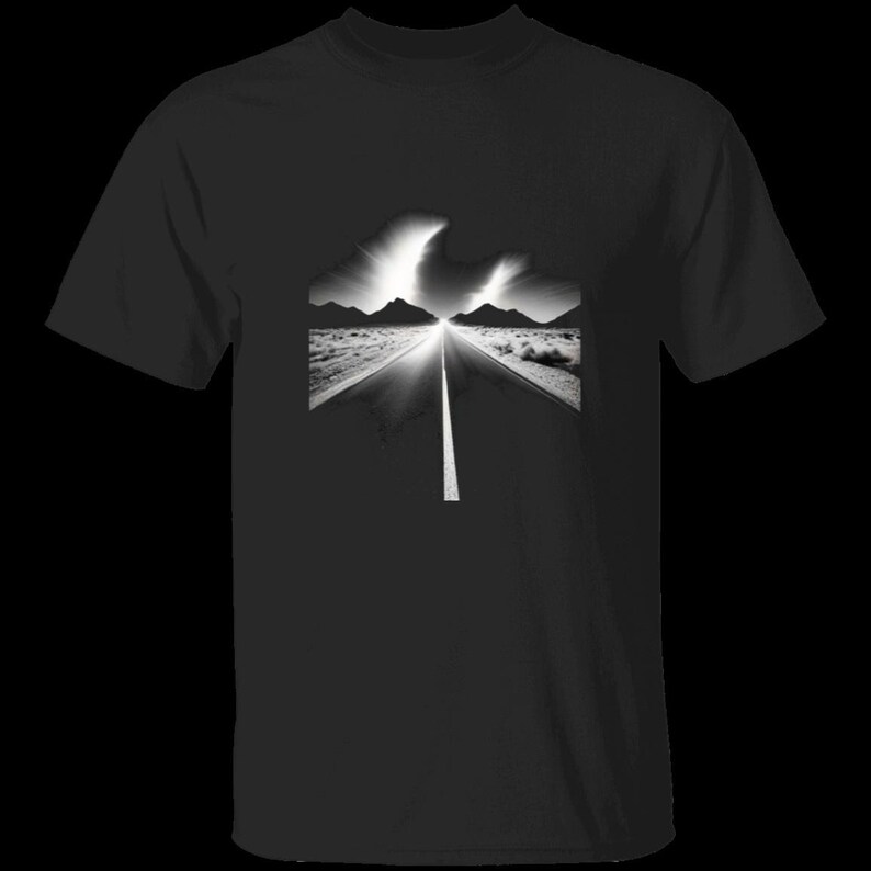 Op de afbeelding: Een zwart T-shirt met korte mouwen en een centrale grafische print van een woestijnweg die naar een verre bergketen leidt onder een heldere, gloeiende lucht. De afbeelding maakt gebruik van een contrastrijke zwart-witstijl.