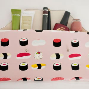 May include: A pink organizer with a sushi pattern, holding beauty products. The organizer has a light-colored interior and features a variety of sushi illustrations. Products include tubes, a mascara, nail polish, and a small jar.
