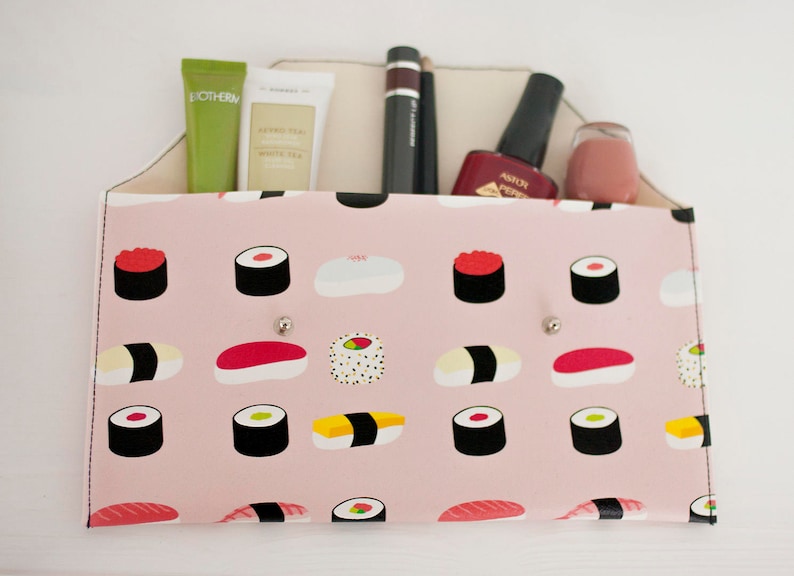 May include: A pink organizer with a sushi pattern, holding beauty products. The organizer has a light-colored interior and features a variety of sushi illustrations. Products include tubes, a mascara, nail polish, and a small jar.